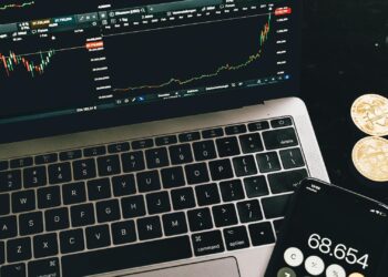 Laptop con gráficas financieras y smartphone sobre escritorio, representando la compra de criptomonedas