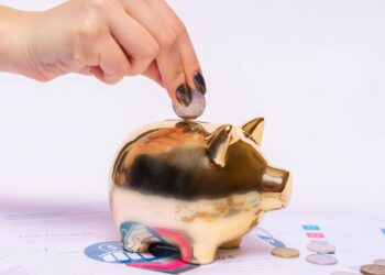 Mano depositando una moneda en una hucha dorada, símbolo de ahorro y cuentas remuneradas en España