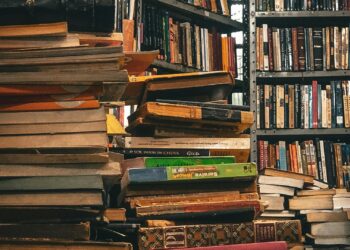 Pila de libros de finanzas personales en una biblioteca como recurso para aprender a invertir
