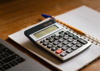 Mesa de trabajo con calculadora, gafas y facturas para facturar sin ser autónomo en España