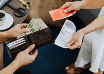 Persona revisando facturas y recibos de domiciliación bancaria sobre una mesa con calculadora
