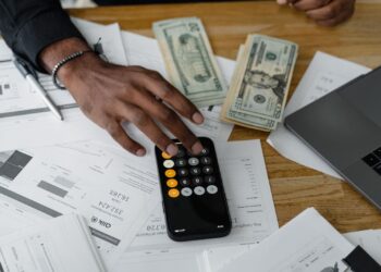 Persona calculando su ratio de endeudamiento con una calculadora sobre documentos financieros