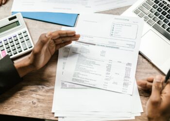 Manos revisando el cuadro de amortización de un préstamo con calculadora y portátil sobre una mesa