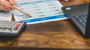 Mano con bolígrafo, calculadora y portátil para compensar pérdidas en bolsa