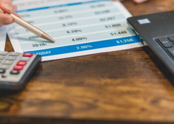 Mano con bolígrafo, calculadora y portátil para compensar pérdidas en bolsa